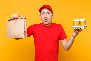 Man in red cap, t-shirt giving fast food order isolated on yellow background. Male employee courier hold paper packet with food, coffee. Products delivery from shop or restaurant to home. Copy space.