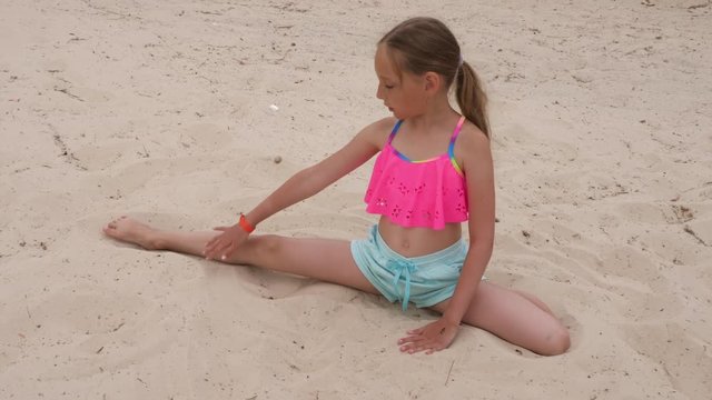 Young sportive girl doing right half split and stretching on sand