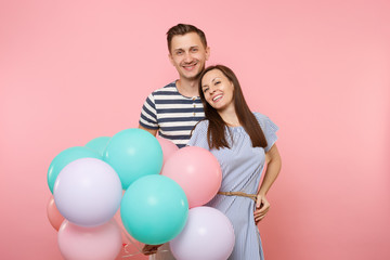 Portrait of young happy smiling couple in love. Woman and man in blue clothes celebrating birthday holiday party on pastel pink background with colorful air balloons. People sincere emotions concept.