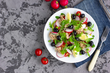Nicoise salad with tuna, egg, cherry tomatoes and black olives on dark grey background. French cuisine. Top view, copy space