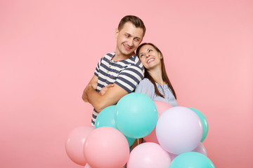 Portrait of couple in love stand back to back. Woman and man in blue clothes celebrating birthday holiday party on pastel pink background with colorful air balloons. People sincere emotions concept.