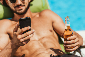 cropped view of man using smartphone and holding bottle of beer
