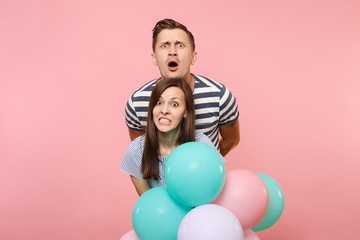 Fototapeta na wymiar Portrait of young fun crazy mad couple in love. Woman and man in blue clothes celebrating birthday holiday party on pastel pink background with colorful air balloons. People sincere emotions concept.