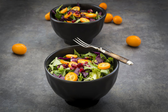 Bowl of mixed green salad with red cabbage, kumquat and pomegranate seeds