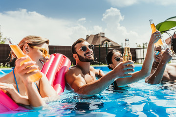 multicultural friends with bottles of beer in swimming pool with inflatable mattress