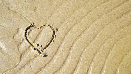 Fototapeta na wymiar Wave marks and a painted heart on a sandy beach.