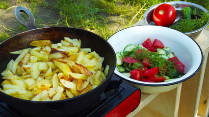 Cooking outdoors.Fried potatoes with salad of fresh vegetables.