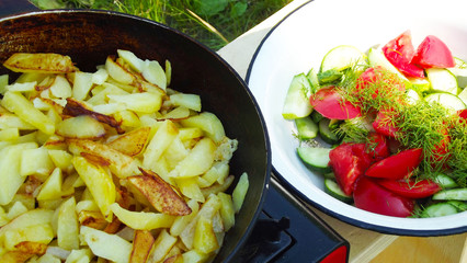 Cooking outdoors.Fried potatoes with salad of fresh vegetables.