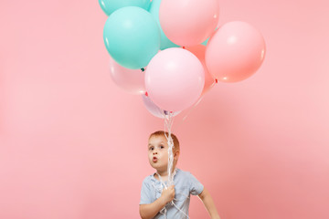 Playful little cute child baby boy holding bunch of colorful air balloons, celebrating birthday holiday party on pastel color pink background. Family day kids children childhood lifestyle concept.