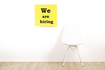 Job recruitment advertisement, WE ARE HIRING text written on yellow wall poster, one empty loft style chair. Human resources campaign to find workers for vacant job. Close up, copy space, background.