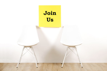 Job recruitment advertisement, JOIN US text written on yellow wall poster, two empty loft style chairs. Human resources campaign to find workers for vacant job. Close up, copy space, background.