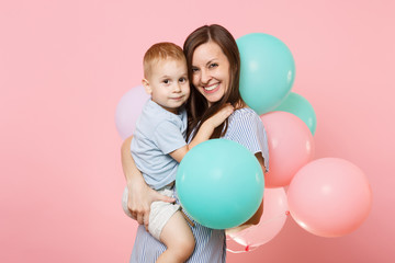 Fototapeta na wymiar Portrait of young happy family, mother keep in arms, have fun, hug child kid son baby boy, celebrating birthday holiday party on pink background with colorful air balloons. Sincere emotions concept.