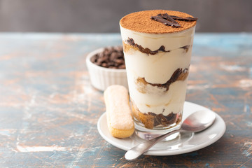 Tiramisu in a glass with coffee beans on grey background. Copy space. Selective focus.