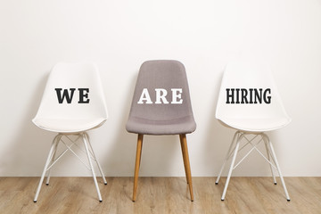 Job recruitment advertisement, WE ARE HIRING text written on three empty loft style chairs white & gray. Human resources campaign to find new workers for vacant job. Close up, copy space, background.