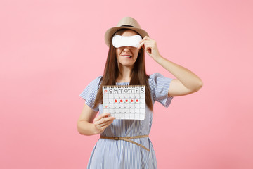 Woman in blue dress, hat holding sanitary napkin, cover eyes, female periods calendar for checking menstruation days isolated on pink background. Medical, healthcare, gynecological concept. Copy space