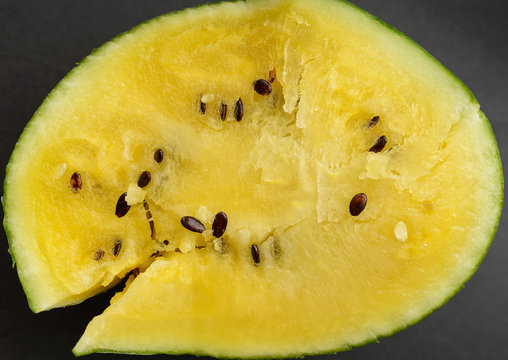 Fresh yellow watermelon slice on dark background.