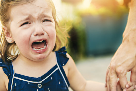 Close Up Portrait Of Crying Little Toddler Girl With Outdoors Background. Child