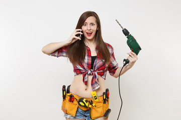 Young energy handyman woman in plaid shirt, kit tools belt full of instruments talking on mobile phone, hold power electric drill isolated on white background. Female in male work. Renovation concept.