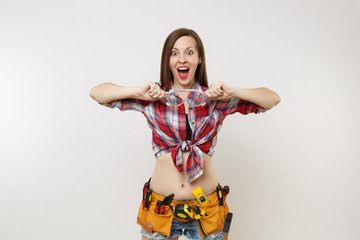 Strong young handyman woman in plaid top shirt, denim shorts, kit tools belt full of instruments in protective goggles isolated on white background. Female in male work. Copy space for advertisement.