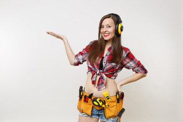 Handyman woman in plaid shirt, denim shorts, noise insulated headphones, kit tools belt full of...