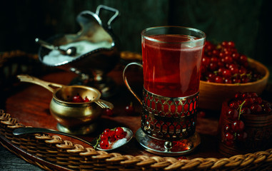 Still life in vintage style. Close up glass and decanter with red current tea or fruit-drink on wicker tray