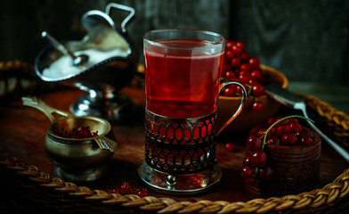 Still life in vintage style. Close up glass and decanter with red current tea or fruit-drink on wicker tray