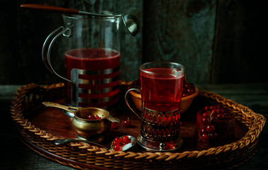 Still life in vintage style. Glass and decanter with red current tea or fruit-drink on wicker tray