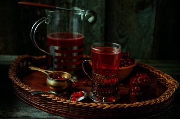 Still life in vintage style. Glass and decanter with red current tea or fruit-drink on wicker tray