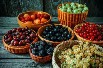 Close up different kind of baskets with fruits on vintage wood background. Red, black and white currant, green and red gooseberry, blackberry and raspberries.