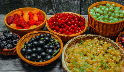 Close up different kind of baskets with fruits in right side of vintage wood background. Red, black and white currant, green and red gooseberry, blackberry and raspberries. Top view