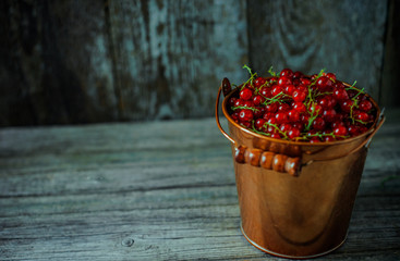 Close up yellow brass bucket with berry of red currant. Which stand in right side on vintage wood background. Top view