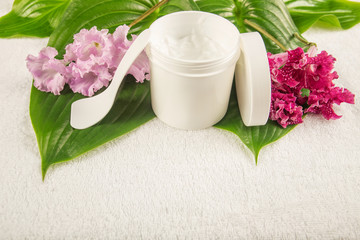 Fototapeta na wymiar green leaf, pink flowers, jar with depilatory cream lie on white towel, spa salon