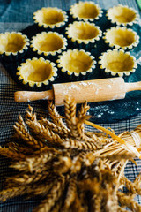 Fototapeta na wymiar Still life in country style. Close up tartlets in baking dishes before bake with spikelets and rolling pin on black stone stand. Top view