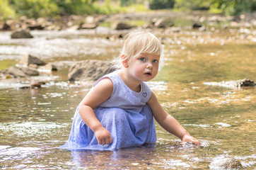 Little girl is playing with water in a river.