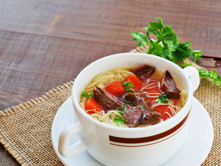 Beef soup with noodles and vegetables in soup bowl over wooden table