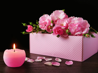 Pink roses over pink gift box with burning candle