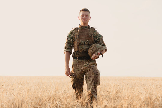 Soldier Man Standing Against A Field. Portrait Of Happy Military Soldier In Boot Camp. US Army Soldier In The Mission. War And Emotional Concept.