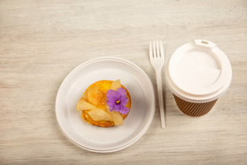 sweet cake is in a plastic plate, the fork and disposable glass lie.on a wooden background, fast food