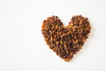 Heart shape created from different, colorful raisins on the white background. Dried grapes. Healthy, sweet food. Empty place for text or logo.