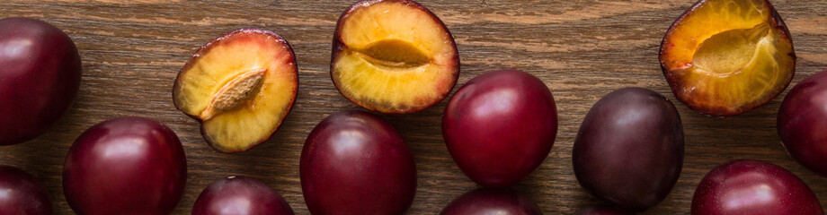 Fototapeta na wymiar Fruit pattern of big, beautiful, fresh, whole and half of plums on brown rustic wooden desk. Healthy sweet food concept. Flat lay. From top view. Banner for website.