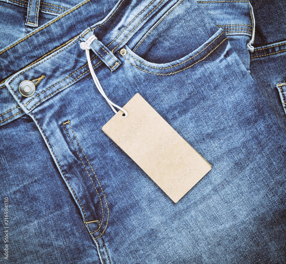 Wall mural fragment of blue jeans with a brown paper tag