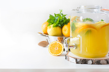 Summer healthy lemonade in big mason jar with lemon, orange and mint on white table. Copy space....