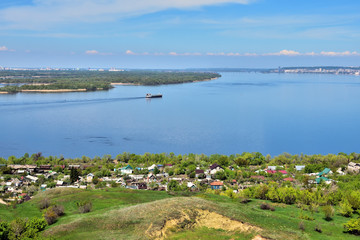 view of the bend of the Volga River from the hill, suburban and urban buildings, coastline, islands, green vegetation, tanker going along the river in the background, Saratov, Russia