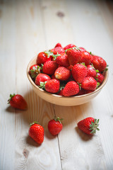 Fresh strawberries in a bowl on wooden table with low key scene.