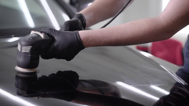 Close up shot of a man waxing black car hood using special machine.