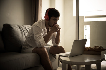 Happy man relaxing on the sofa listening to music with laptop at home