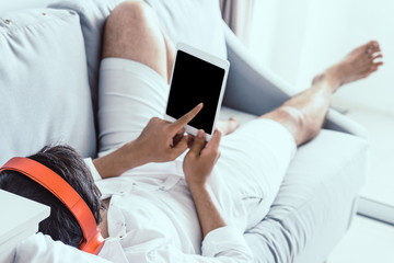 Happy man in headphones with tablet computer relaxing on the sofa in bedroom