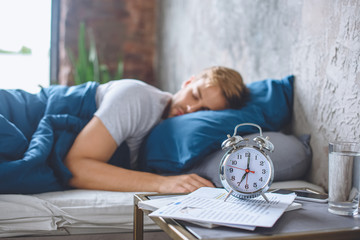 selective focus of alarm clock and sleeping man in bed behind