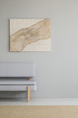 Real photo of a minimal living room interior with a burlap artwork above a gray couch. Place for...