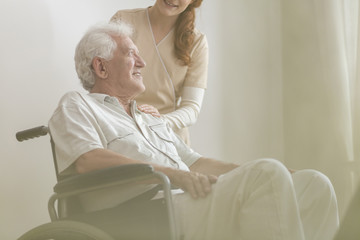 Low angle on smiling and happy disabled elderly man in the wheelchair and caregiver
